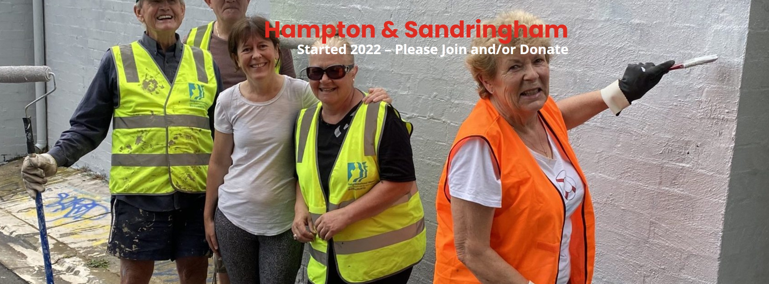 Group of neighbourhood volunteers in casual clothing and high viz vests painting over graffiti in a lane way. All smiling and happy.